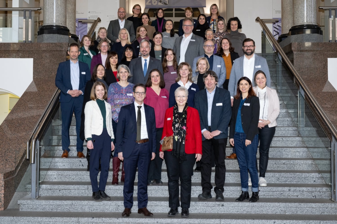 Circa 30 Menschen stehen auf einer Treppe und lachen in die Kamere